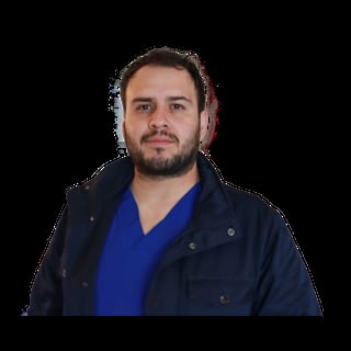 Portrait of a man with dark hair and beard wearing a navy jacket over a blue shirt against a black background