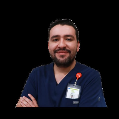 Male healthcare professional in dark blue scrubs wearing an ID badge, smiling with arms crossed against a black background