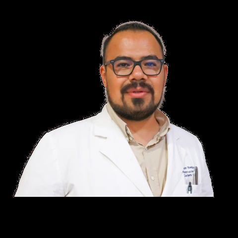Professional headshot of a man with dark hair and goatee wearing glasses and a white lab coat over a beige shirt