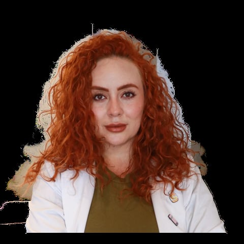 Woman with long curly copper-red hair wearing a white blazer over an olive green top, posed against a black background