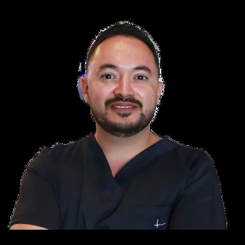 Man with beard wearing black scrubs against dark background, professional headshot