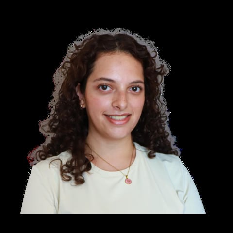 Portrait of a smiling young woman with long curly brown hair wearing a white t-shirt and a pink pendant necklace against a black background