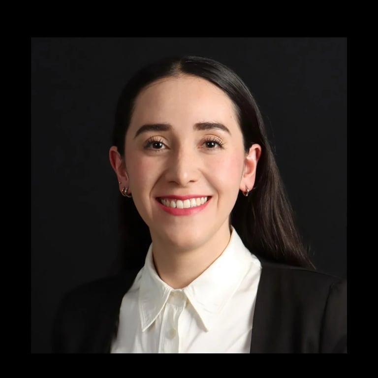 Professional headshot of a woman with long dark hair, wearing a black blazer and white collared shirt, smiling against a dark background