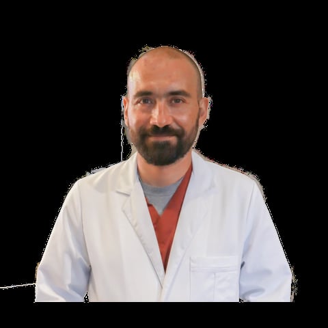 Male healthcare professional with beard wearing white lab coat and red shirt, smiling at camera against black background
