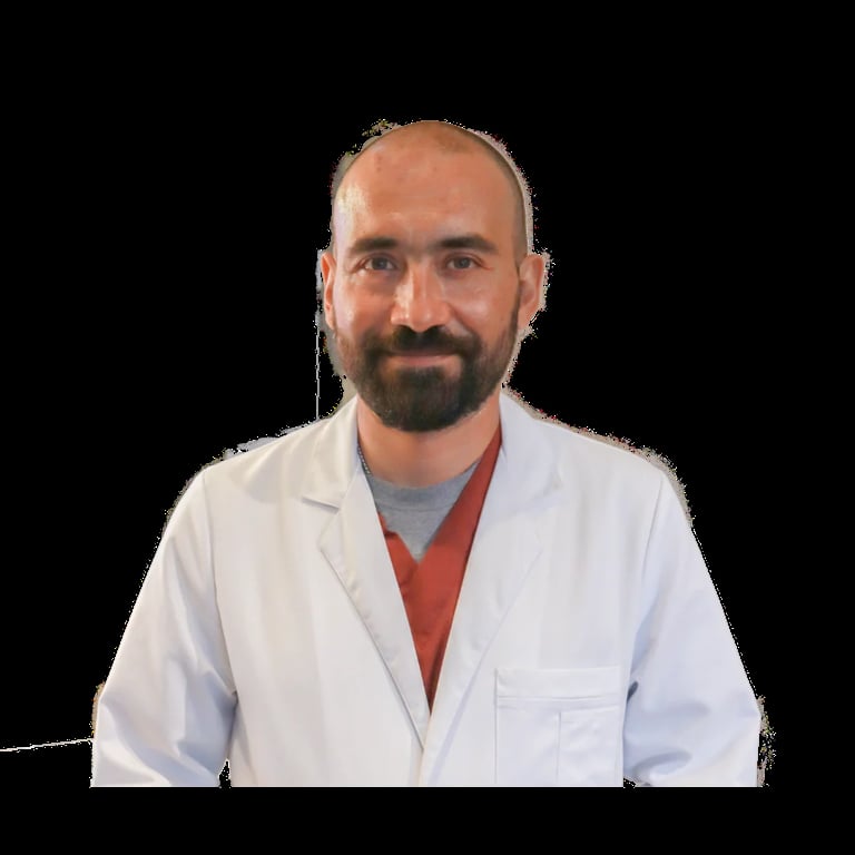 Male healthcare professional with beard wearing white lab coat and red shirt, smiling at camera against black background