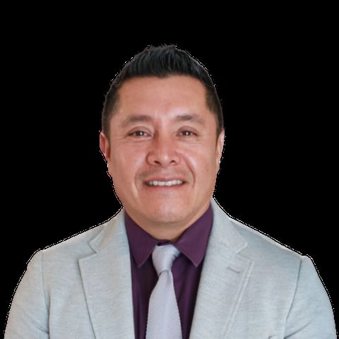 Professional headshot of a man in a light gray blazer and purple dress shirt smiling at the camera against a black background