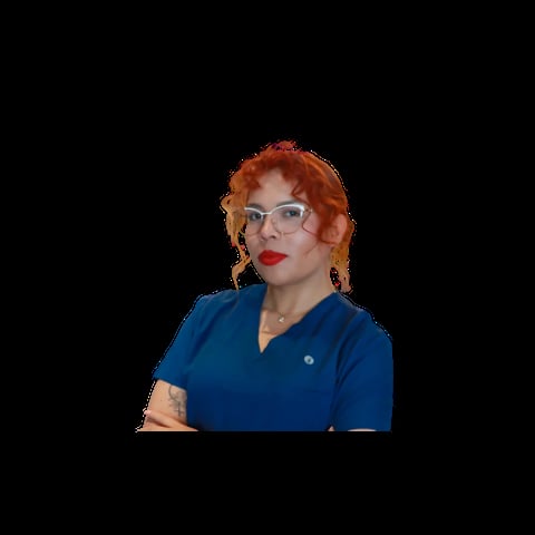 Woman with curly red hair and glasses wearing a blue medical scrub top against a black background