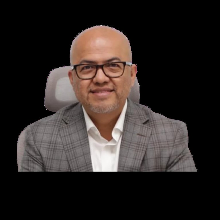 Professional headshot of a bald man with glasses wearing a gray plaid blazer and white shirt, seated in an office chair