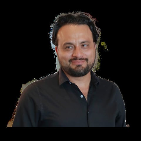Headshot of a man with dark hair and beard wearing a black collared shirt against a black background
