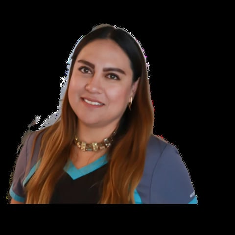 Woman with long reddish-brown hair, wearing a blue cardigan over a black shirt with turquoise trim and a gold chain necklace, smiling at the camera against a black background