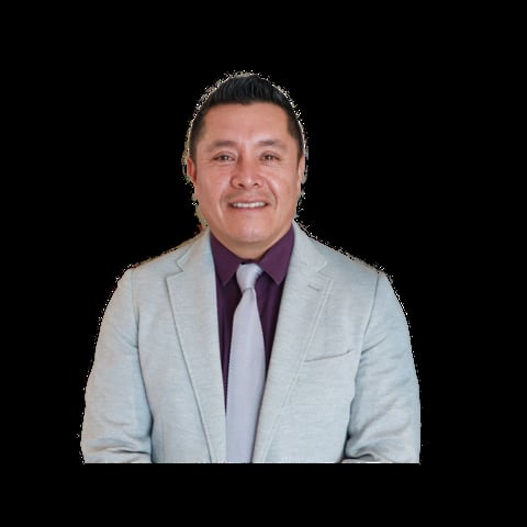 Professional headshot of a smiling man wearing a light blue blazer over a dark purple shirt and tie