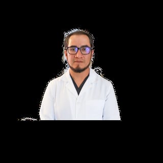Man wearing blue-framed glasses and white lab coat with dark undershirt against black background