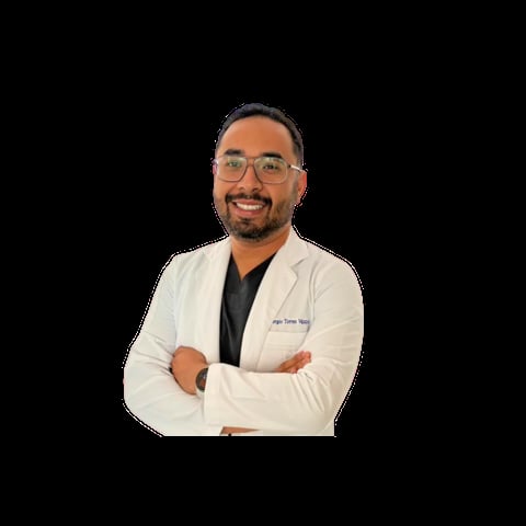Male healthcare professional wearing white lab coat and glasses, smiling with arms crossed against black background